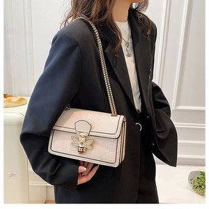 Close-up of beige embossed leather bag with golden bee clasp and chain strap