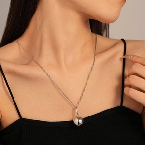 Collier minimaliste en acier inoxydable avec pendentif boule poli porté par un mannequin