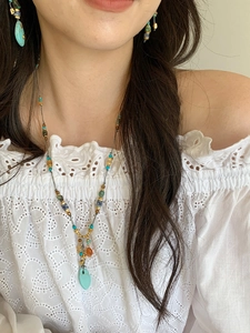Detail of bohemian turquoise beaded necklace and matching earrings on a white lace top