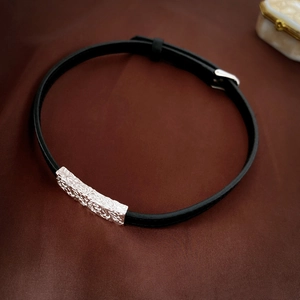 Detail view of a black leather bracelet with an ornate silver metal buckle on brown silk