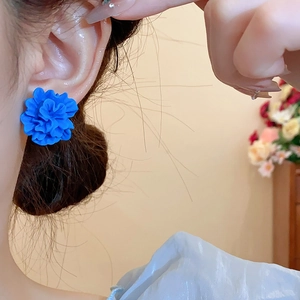 Gros plan de boucles d'oreilles fleurs en résine bleu klein mat portées par un mannequin