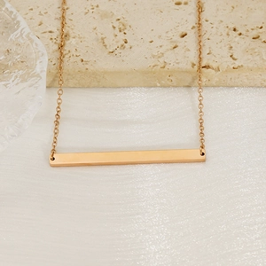 Detailed view of a gold rectangular bar pendant necklace on a refined stone texture