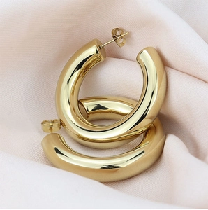 Macro view of polished gold C-shape hoop earrings on soft pink silk fabric background