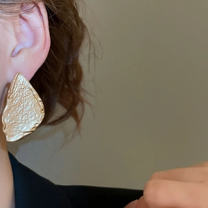 Close-up of gold textured geometric triangle earrings with hammered metal finish on model