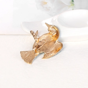 Golden bird brooch pin with back clasp detail on a textured minimalist background