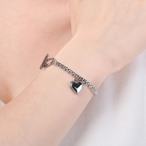 Dettaglio di un bracciale argento con ciondolo a cuore, chiusura a T e maglia a catena
