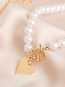 Detail of baroque pearl bracelet with gold heart pendant and OT clasp on silk fabric