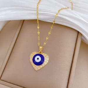 Gold heart necklace with blue evil eye pendant and cubic zirconia on beige jewelry pad