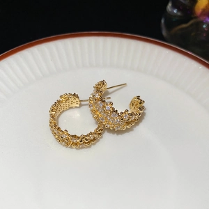 Macro shot of gold C-shaped earrings with intricate floral textures and cubic zirconia
