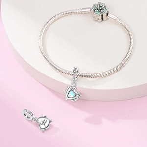 Detailed view of silver heart charm with light blue gemstone and World Peace engraving