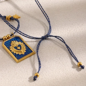 Detail of square blue enamel pendant with gold sacred heart on woven cord necklace