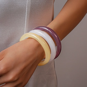 Detailed view of three smooth resin bangles in purple, white, and cream on a wrist