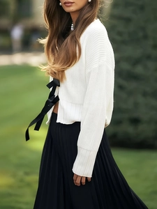 Dettaglio del cardigan in maglia bianca con fiocchi neri e gonna a pieghe