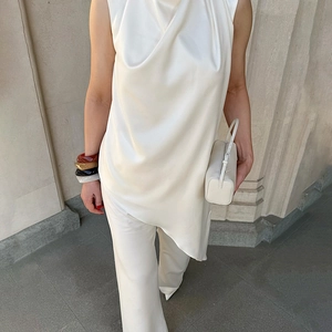 Detail of white sleeveless asymmetric satin top with button neck and matching trousers