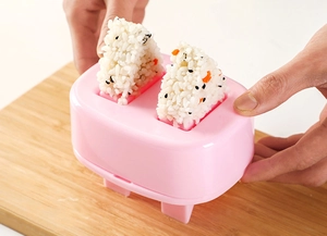 Pink toaster-shaped rice ball mold creating two triangular sushi on a wooden board