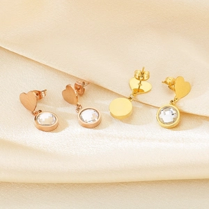 Detail of rose gold and gold heart-shaped earrings with clear crystals on silk