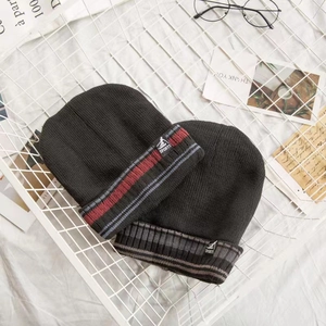 Close-up of black knitted beanies with ribbed cuffs and sports patches on grid background