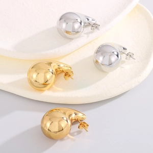 Detailed view of glossy gold and silver teardrop earrings on a white ceramic tray