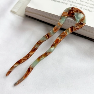 Detailed view of wavy U-shaped acetate hair pins with marble texture on white fabric