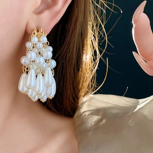 Close-up of golden cluster tassel earrings with white pearls worn by a model