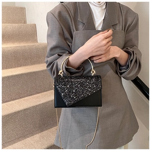 Detail of black sequin crossbody bag with gold ring handle and metal chain strap on model