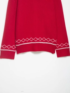 Dettaglio di maglione rosso in maglia con motivo a rombi bianchi e bordi a coste