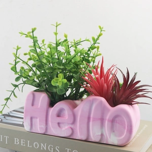 Macro detail of 'Hello' letter flower pot with pink marble texture and faux succulents