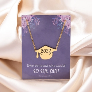 Macro view of gold 2022 graduation cap necklace on silk with inspirational card display