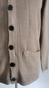 Detail of khaki knit cardigan showing black buttons, ribbed texture, and side pocket
