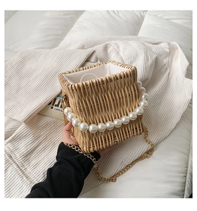 Detailed view of woven straw bag featuring elegant pearl handle and gold chain strap