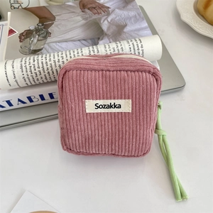 Detail of pink corduroy makeup bag with green zipper puller on a white desk