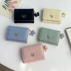 Women's tri-fold short wallets with bow hardware in pastel colors shown on a desk