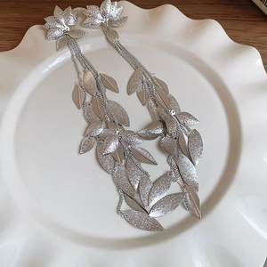 Détail de boucles d'oreilles pampilles feuilles argentées sur une assiette blanche en céramique
