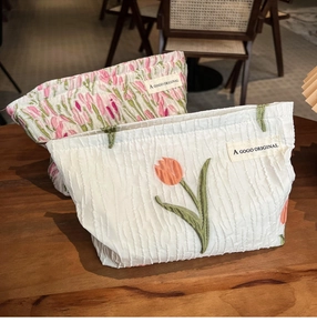 Detail of tulip embroidery on canvas cosmetic bags with woven brand labels on wood