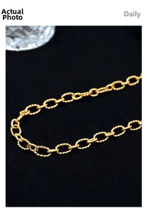 Macro shot of gold twisted oval chain links showing detailed spiral texture on black fabric