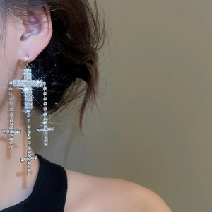 Close-up of dangling cross tassel earrings with sparkling rhinestones worn by a model