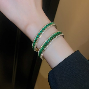 Detail view of gold bangles with emerald green stones in round and square cuts
