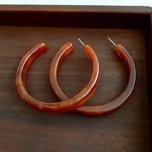 Close-up of amber resin C-shaped hoop earrings with silver pins on a wooden tray