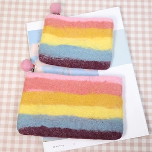 Rainbow striped wool felt coin purse with pink pompom zipper on a checkered tablecloth