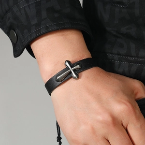 Close-up of a black braided leather bracelet featuring an antique silver cross charm