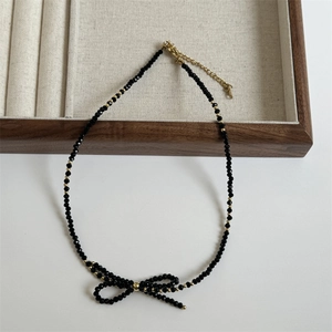 Detail of black faceted bead necklace with woven bow pendant and gold extender chain