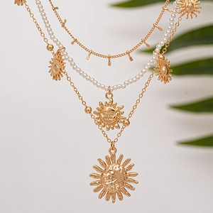 Detail of layered gold necklaces with sunflower face pendants and faux pearl accents