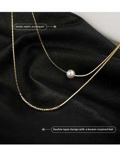 Close-up of double-layer gold necklace with a white pearl and textured metal tube