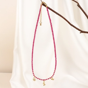 Detail of bohemian fuchsia bead necklace with gold star and crown charms on branch