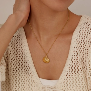 Detail of a gold seashell pendant on a delicate bead chain worn by a female model