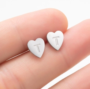 Gros plan sur un clou d'oreille en forme de cœur en acier avec lettre T gravée à la main