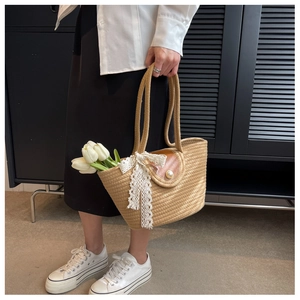 Detail of straw tote bag with brown faux leather flap, pearl clasp and white lace bow