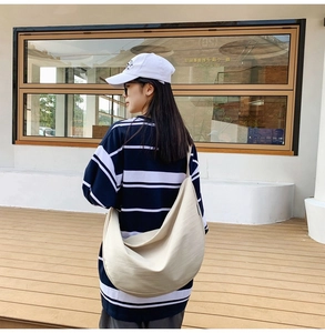 Detailed side view of a large beige crescent oxford bag worn by a model in a modern setting