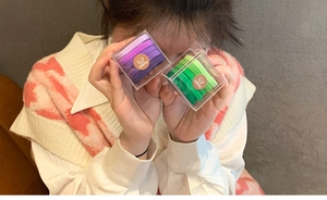 Detail showing hand holding transparent box of purple and green gradient elastic hair ties