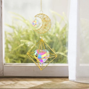 Detail of suncatcher featuring golden metal moon and iridescent crystal heart hanging by window